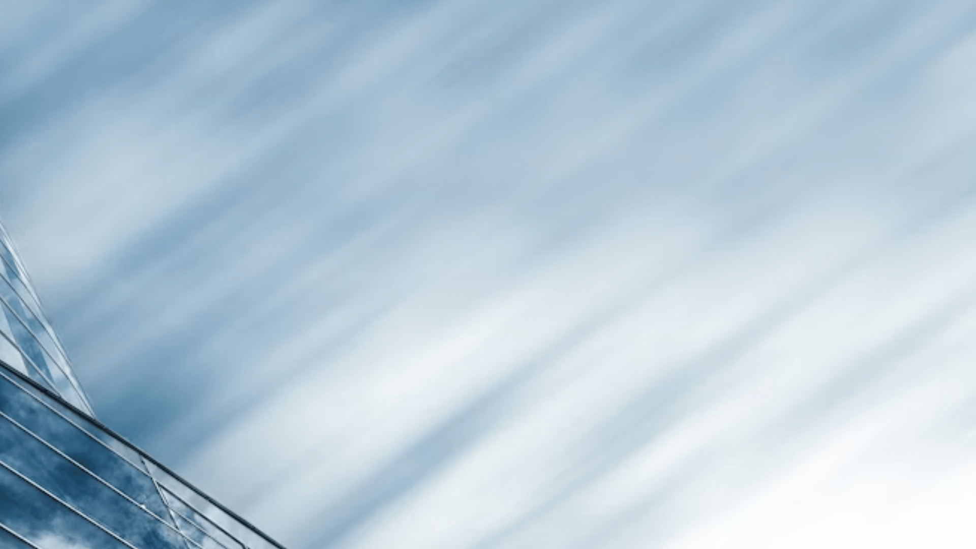 Abstract upward angle of a glass building edge against a blurred sky, conveying direction, momentum, and forward leadership.