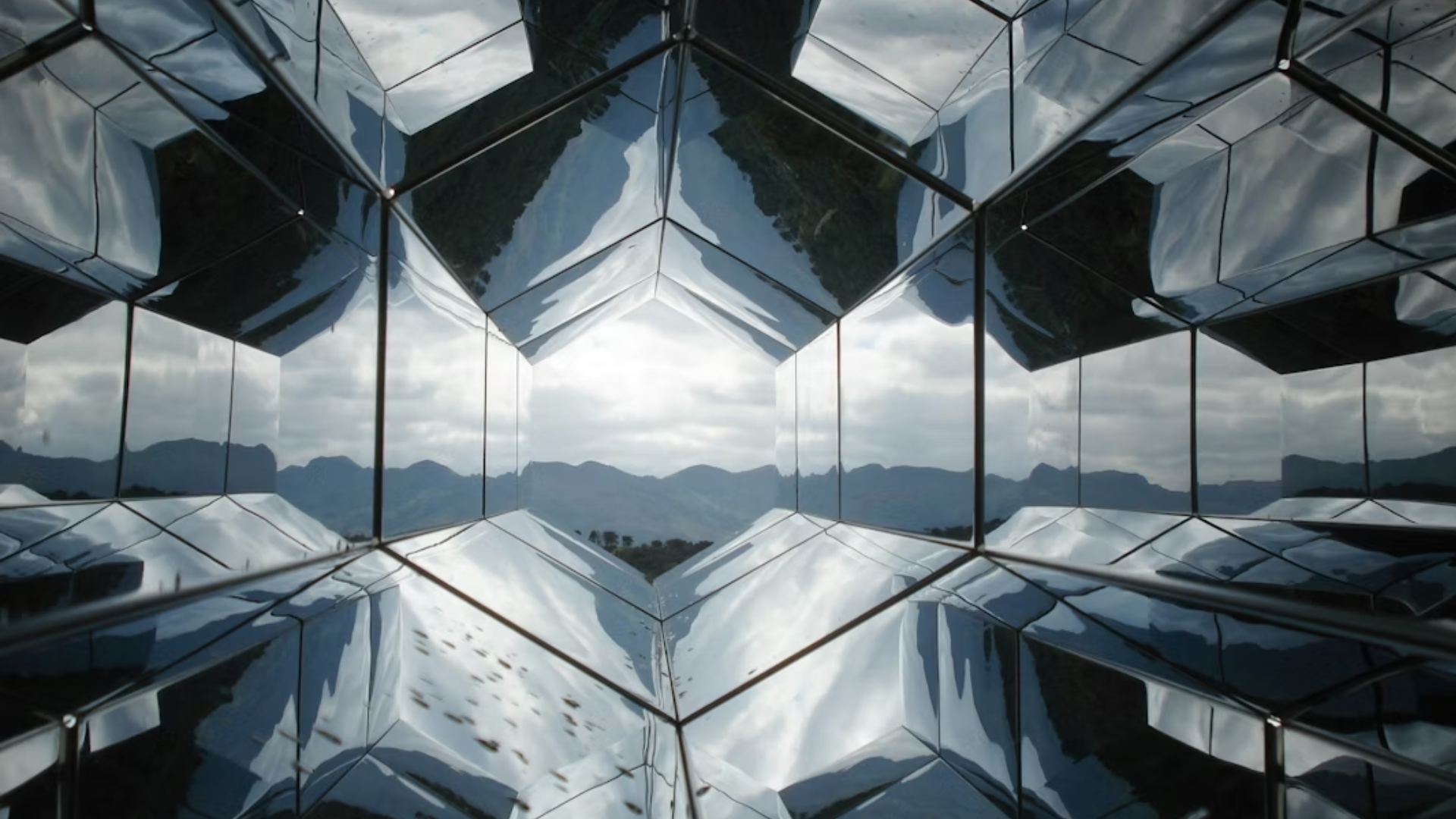 Symmetrical mirrored glass structure reflecting a mountainous landscape, creating a geometric, faceted view that emphasizes precision and complexity.